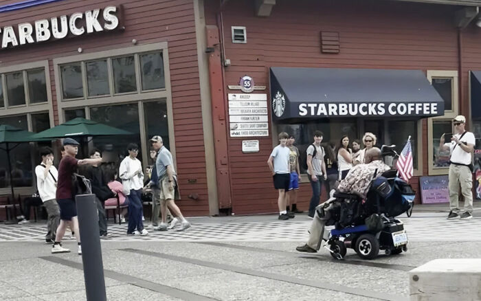 Crowded street scene outside Starbucks with a man in a motorized wheelchair holding a small American flag. Crowded street scene outside Starbucks with a man in a motorized wheelchair holding a small American flag.