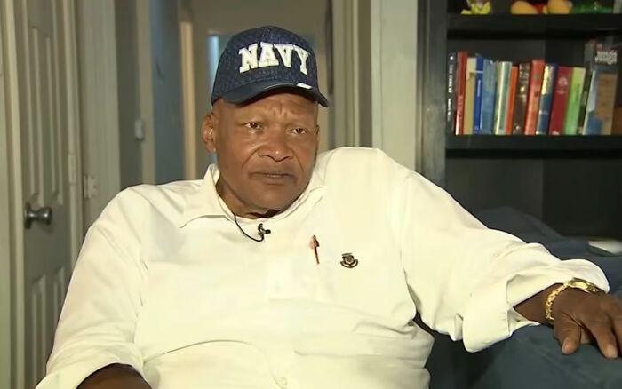 Black disabled veteran wearing navy cap and white shirt, seated in a home setting discussing proof of service incident. Black disabled veteran wearing navy cap and white shirt, seated in a home setting discussing proof of service incident.
