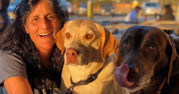 Astronaut smiling with her two dogs during a warm reunion after a long homecoming, bathed in golden sunlight outdoors.