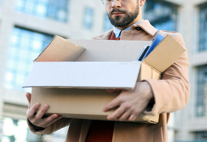 Man holding a box of personal items outside office, facing discipline again for inappropriate work comments.