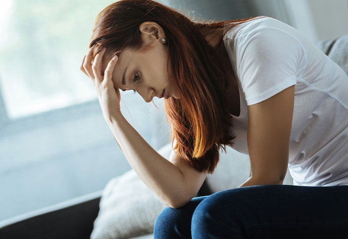 Woman sitting on a couch with head in hand, showing concern about husband facing discipline for inappropriate work comments