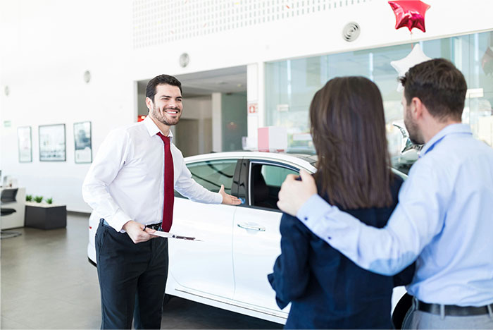 Husband and wife at car dealership, husband pulling wife away before she can show him the car she wants