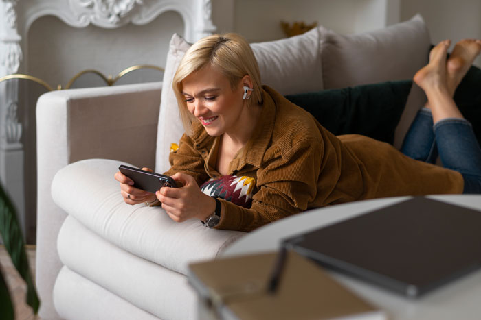 Woman lying on couch smiling at phone, representing stay-at-home mom and teen job discussions at home.