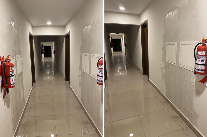 Long indoor hallway with water damage on walls and fire extinguisher, showing nature's impact in wild conditions.