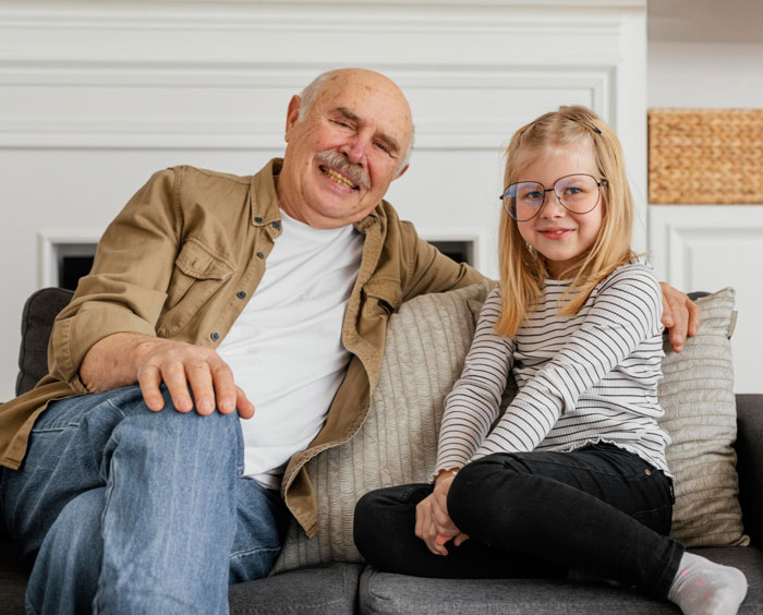 Elderly grandpa sitting with young girl on couch, highlighting years spent taking care of grandpa by family member. - 1
