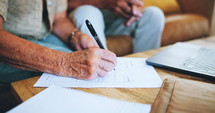 Elderly grandpa signing documents at a table with a laptop nearby, symbolizing caregiving and family demands. - 9