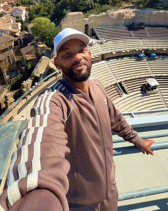 Will Smith taking a selfie in a track suit overlooking an empty amphitheater with AI-faked crowds controversy. Will Smith taking a selfie in a track suit overlooking an empty amphitheater with AI-faked crowds controversy.