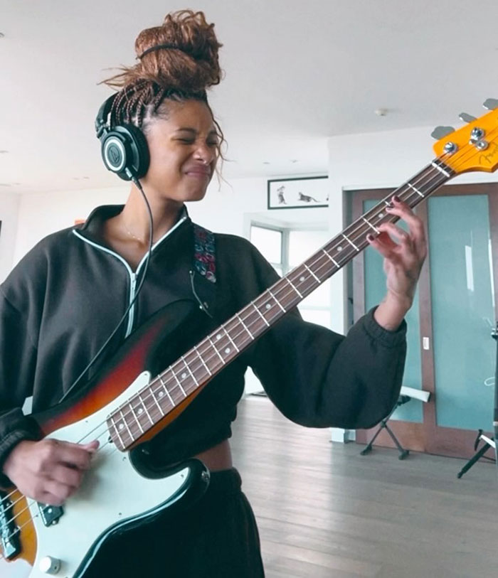 Will Smith and Jada Pinkett's daughter playing guitar with headphones on, showing intense expression indoors.