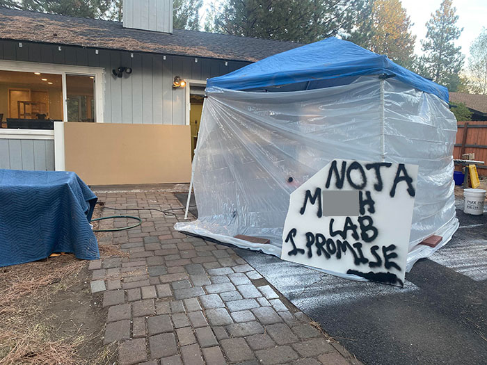 Outdoor setup with plastic-covered tent and witty black spray-painted warning sign, showcasing cleverness and humor.