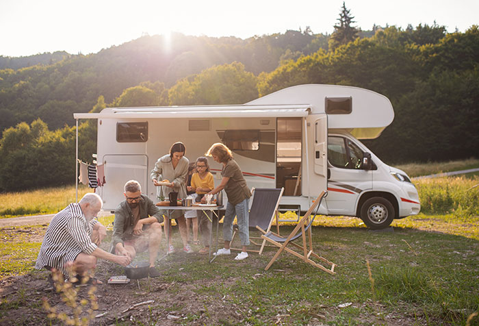 Group camping by RV in nature, woman and friends preparing food with husband nearby during outdoor trip tensions.