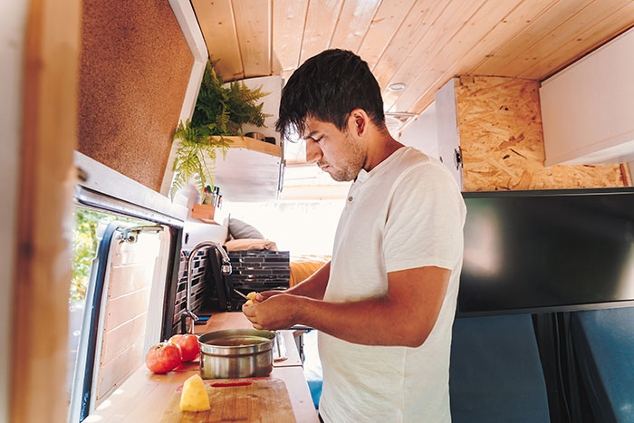 Man preparing food in camper van kitchen, illustrating tensions and regrets during a trip with friend and husband.