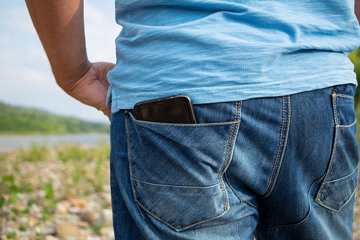 Man wearing blue shirt and jeans with phone in back pocket standing outdoors by a river, capturing trip tensions.