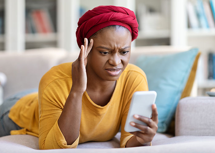 Woman checks boyfriend&rsquo;s phone looking upset and regretful while lying on couch in a living room setting.