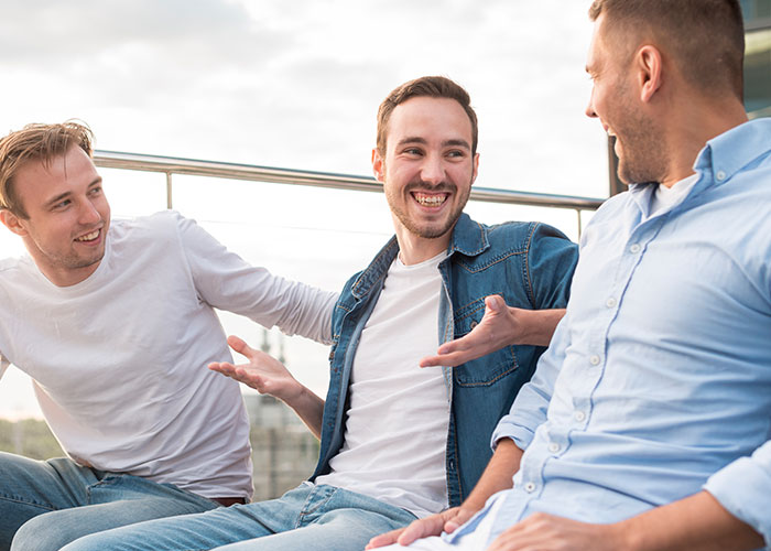 Three men sitting outdoors, smiling and chatting, depicting a casual moment related to woman checking boyfriend's phone after jealous freak-out.