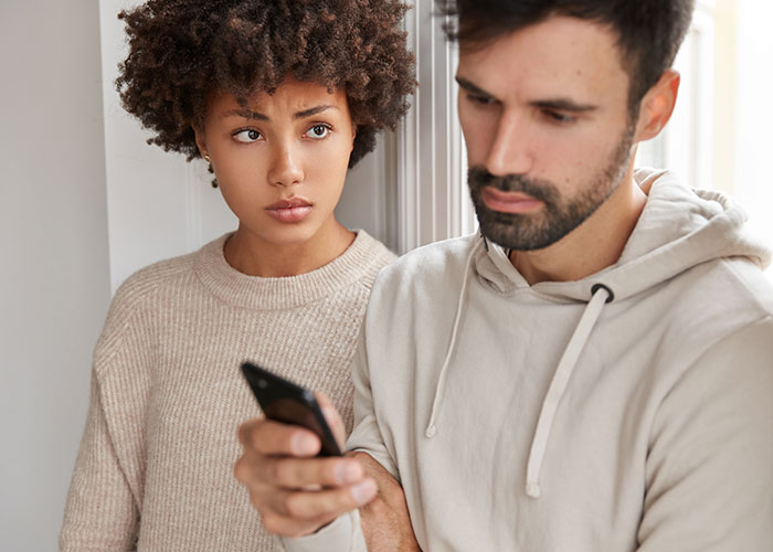Woman looks concerned as she checks boyfriend&rsquo;s phone after jealous freak-out, feeling regret in a tense moment.