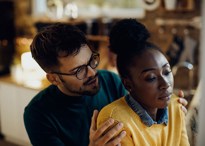Woman checks boyfriend&rsquo;s phone after jealous freak-out, looking regretful with tense body language indoors.