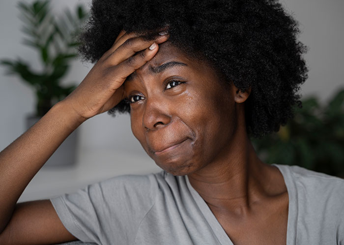 Woman experiencing regret after checking boyfriend&rsquo;s phone, showing emotional distress indoors with hand on forehead.