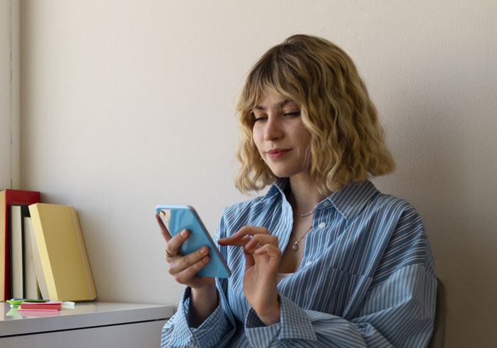 Woman in a striped shirt using a smartphone, representing netizens reacting to AI boyfriend proposal news online.