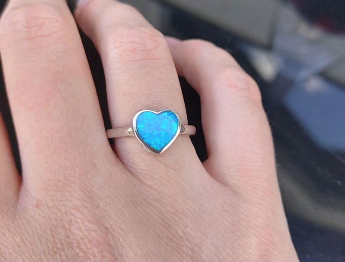 Close-up of a hand wearing a heart-shaped blue ring symbolizing a woman saying yes to her AI boyfriend&rsquo;s proposal.