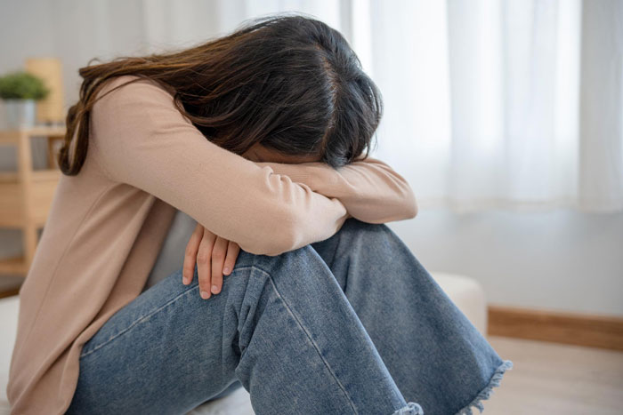 Woman sitting on floor with head resting on arms, reflecting emotions related to AI boyfriend proposal and netizens' reactions.
