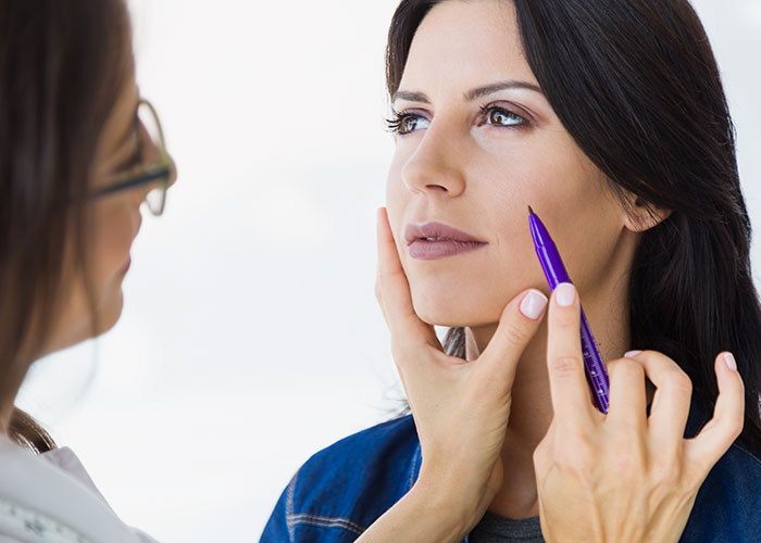 Woman getting facial assessment from doctor, illustrating concerns about women who get facelifts at 28 years old. Woman getting facial assessment from doctor, illustrating concerns about women who get facelifts at 28 years old.
