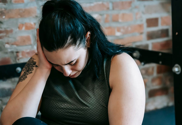 Woman sitting indoors looking down, appearing upset after being told to lose weight by a good friend.