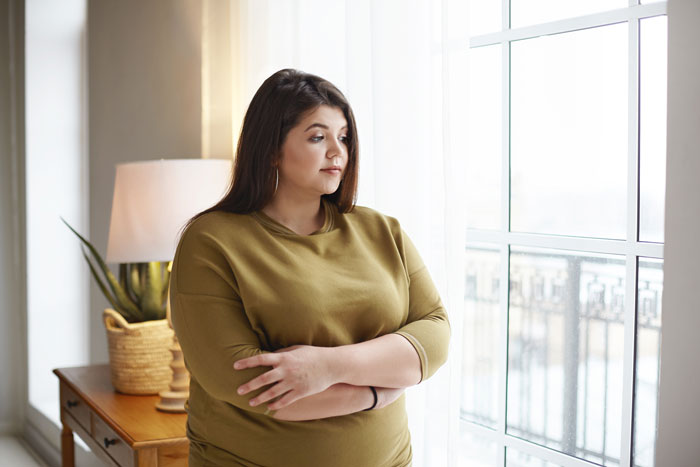 Woman in a green shirt standing by a window, looking thoughtful, reflecting on a reunion with a good friend after years.