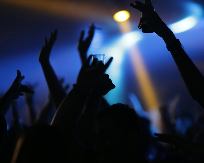 Silhouettes of people raising hands and drinks in a dark club setting, related to woman warning after trafficking rescue. Silhouettes of people raising hands and drinks in a dark club setting, related to woman warning after trafficking rescue.