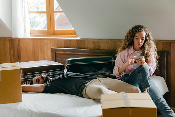 Woman agrees to temporary houseguest, looking frustrated while man relaxes on bed surrounded by packed boxes and suitcases. Woman agrees to temporary houseguest, looking frustrated while man relaxes on bed surrounded by packed boxes and suitcases.