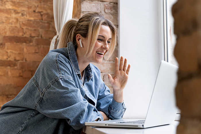 Woman agreeing to temporary houseguest, smiling while video chatting on laptop near a window in cozy room Woman agreeing to temporary houseguest, smiling while video chatting on laptop near a window in cozy room
