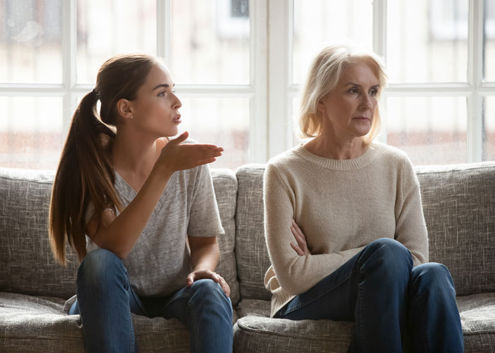 Young woman feeling needy and hurt as parents lose interest after she moves out, sitting tense on a couch indoors. Young woman feeling needy and hurt as parents lose interest after she moves out, sitting tense on a couch indoors.