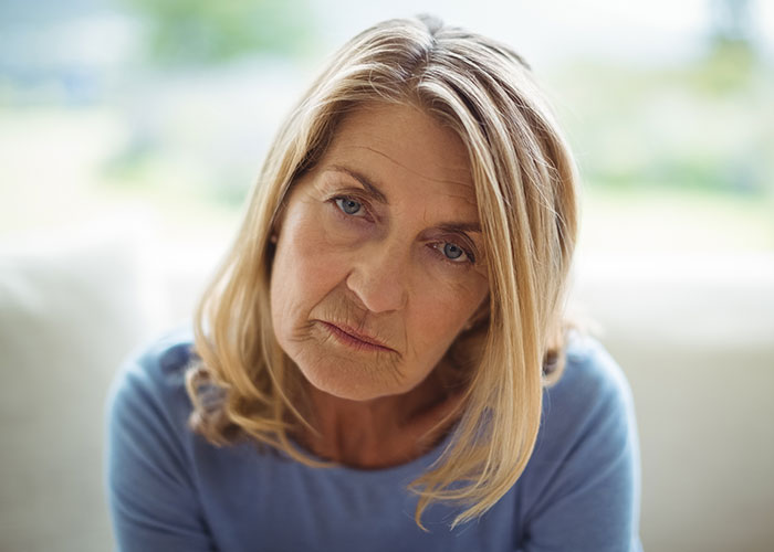 Sad middle-aged woman with blonde hair looking down, reflecting on parents breaking daughter's heart after moving out. Sad middle-aged woman with blonde hair looking down, reflecting on parents breaking daughter's heart after moving out.