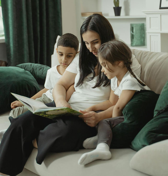 Woman reading a book with two children on a couch, highlighting challenges of babysitting her autistic nephew.