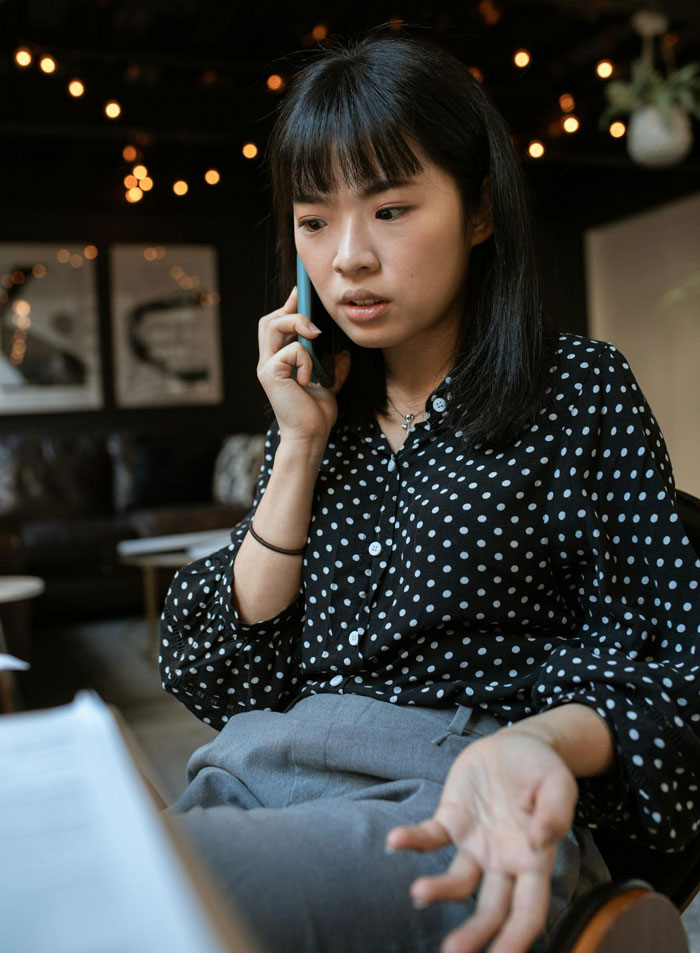 Young woman in polka dot blouse talking on phone, appearing frustrated while discussing babysitters and living wage.