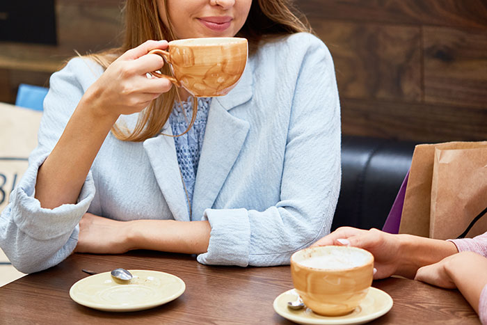 Woman sipping coffee at a table, seeking family support but facing drama after sister-in-law feels outshined