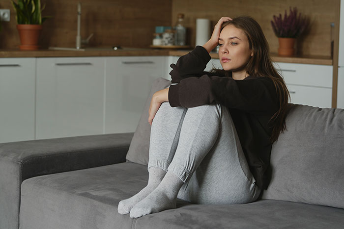 Young woman in casual clothes sitting on a couch looking distressed, needing support from family after devastating news.