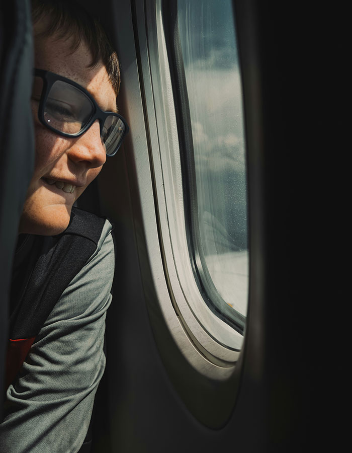Child looking out airplane window during flight, illustrating passenger experience with bored child sparking debate on flight.