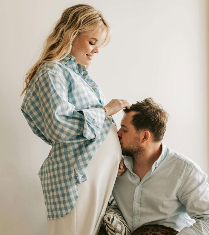 Pregnant wife smiling as husband kisses her belly, reflecting postpartum trip and family bonding moments.
