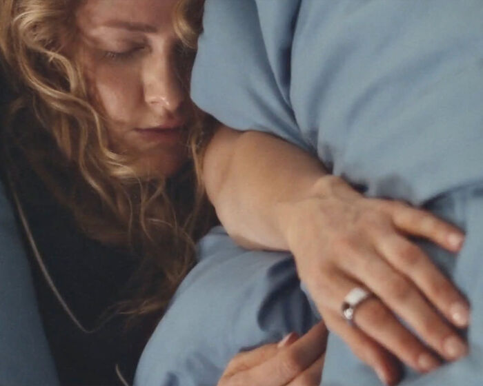 Woman wearing a smart ring lying in bed, resting with eyes closed, illustrating early illness detection technology.