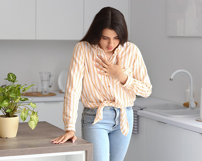 Woman with hand on chest in kitchen, illustrating smart ring detected major illness before doctor's diagnosis.
