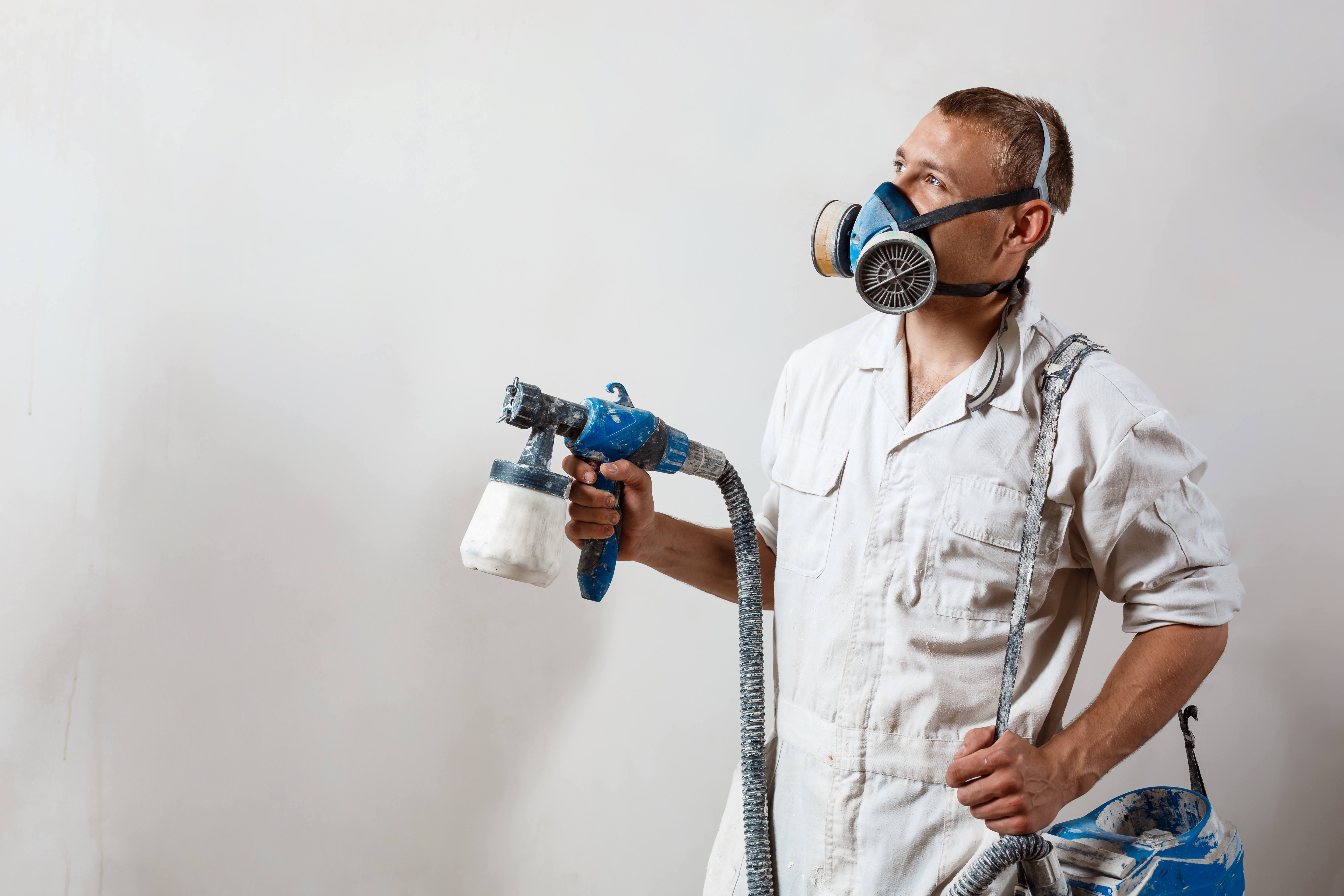 Painter wearing protective mask holding spray gun, working on a house renovation with unexpected surprise potential.