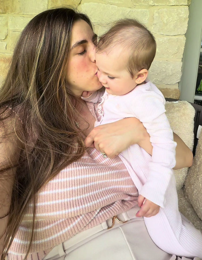 Woman with long hair holding and kissing baby, illustrating challenges of being a working mom in the U.S. Woman with long hair holding and kissing baby, illustrating challenges of being a working mom in the U.S.