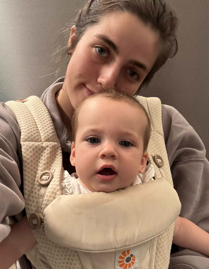 Woman and baby in a carrier, illustrating the challenges of being a working mom in the U.S. in a candid moment. Woman and baby in a carrier, illustrating the challenges of being a working mom in the U.S. in a candid moment.