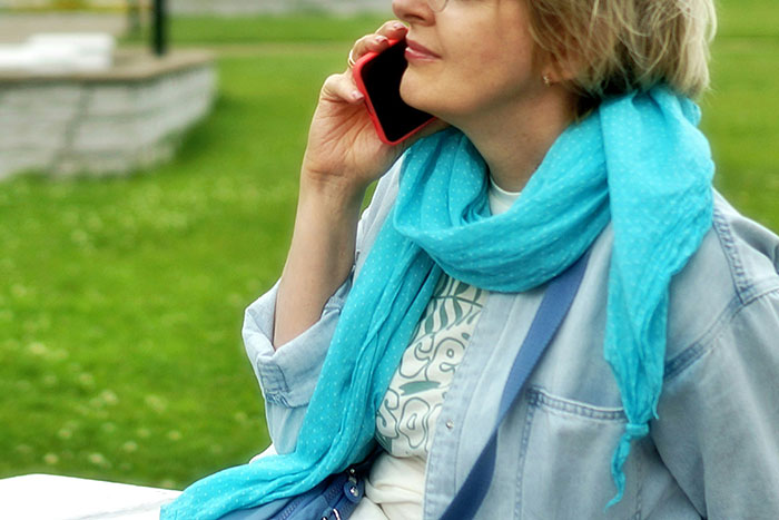 Woman in a blue scarf talking on phone outdoors, illustrating students telling hilariously bad lies on college applications.