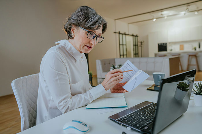 Woman in glasses reviewing documents at desk with laptop, illustrating hilariously bad lies students use on college applications.