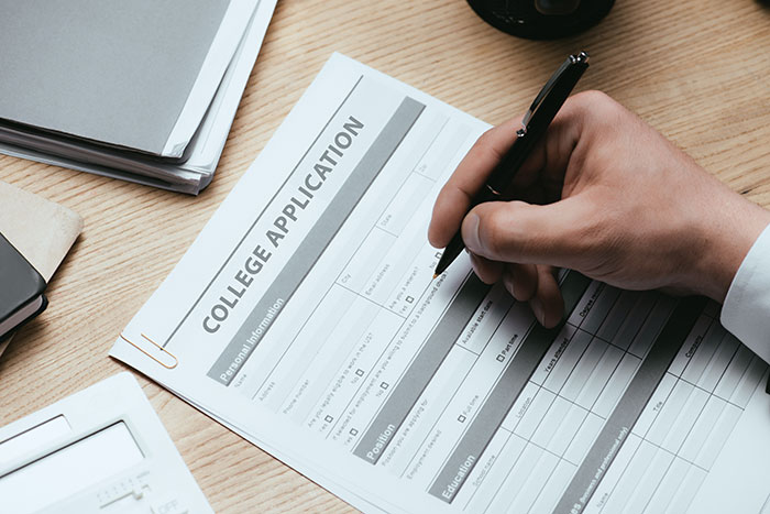 Person filling out a college application form with a pen on a wooden desk, illustrating student lies on applications.