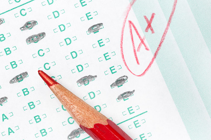 Red pencil pointing to multiple-choice answers on test paper marked with a large red A plus grade, highlighting student lies.