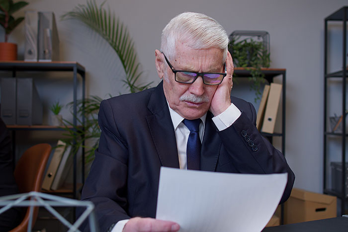 Elderly man in suit and glasses looking stressed while reviewing college application with hilariously bad lies.