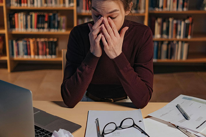 Stressed student in library surrounded by papers and laptop after bad lies on college applications failed.