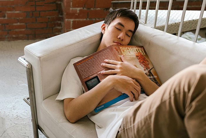 Young student asleep on a couch holding a chemistry book, representing bad lies students put on college applications.